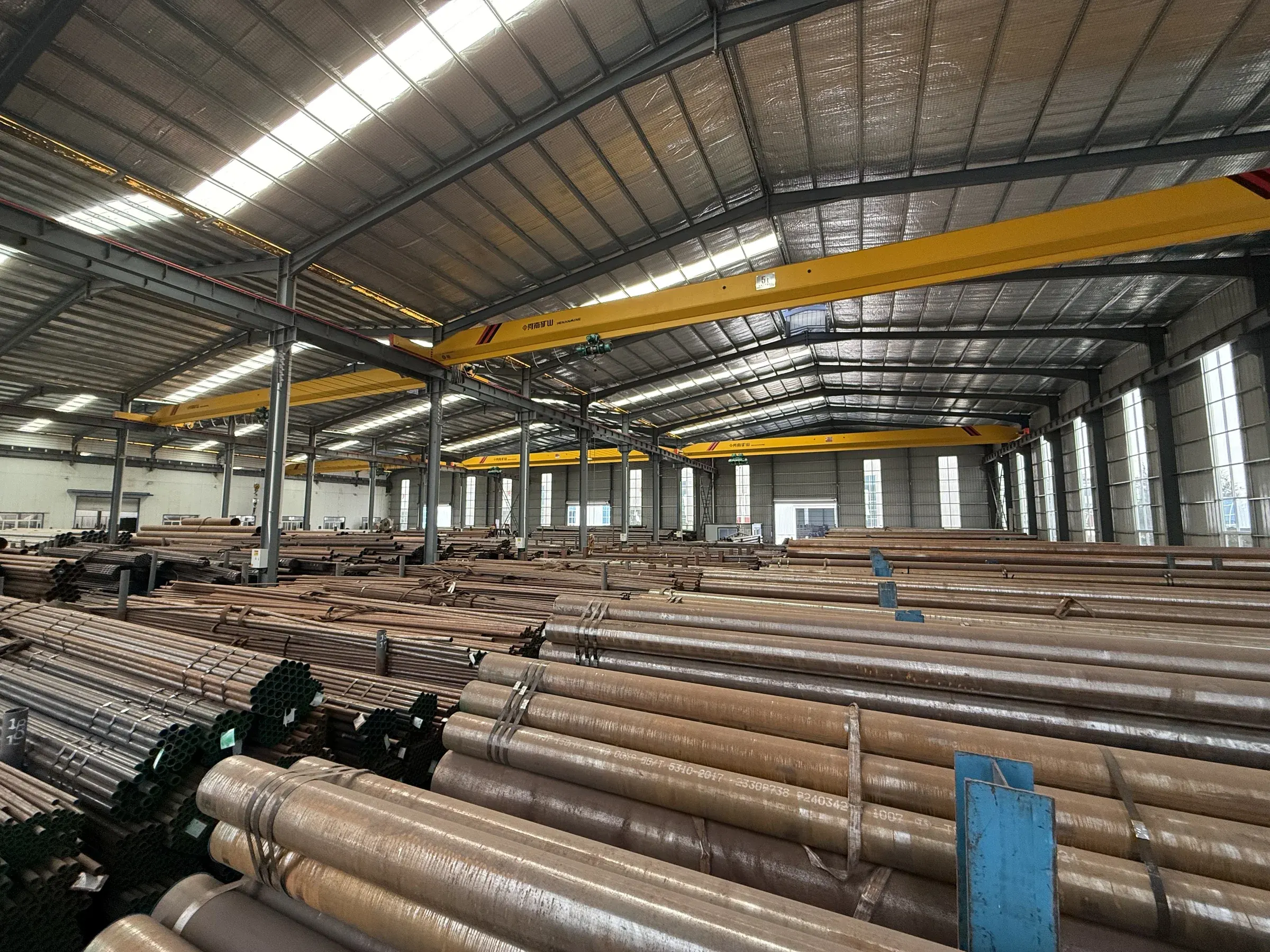 Rows of steel pipes stored beneath an overhead crane