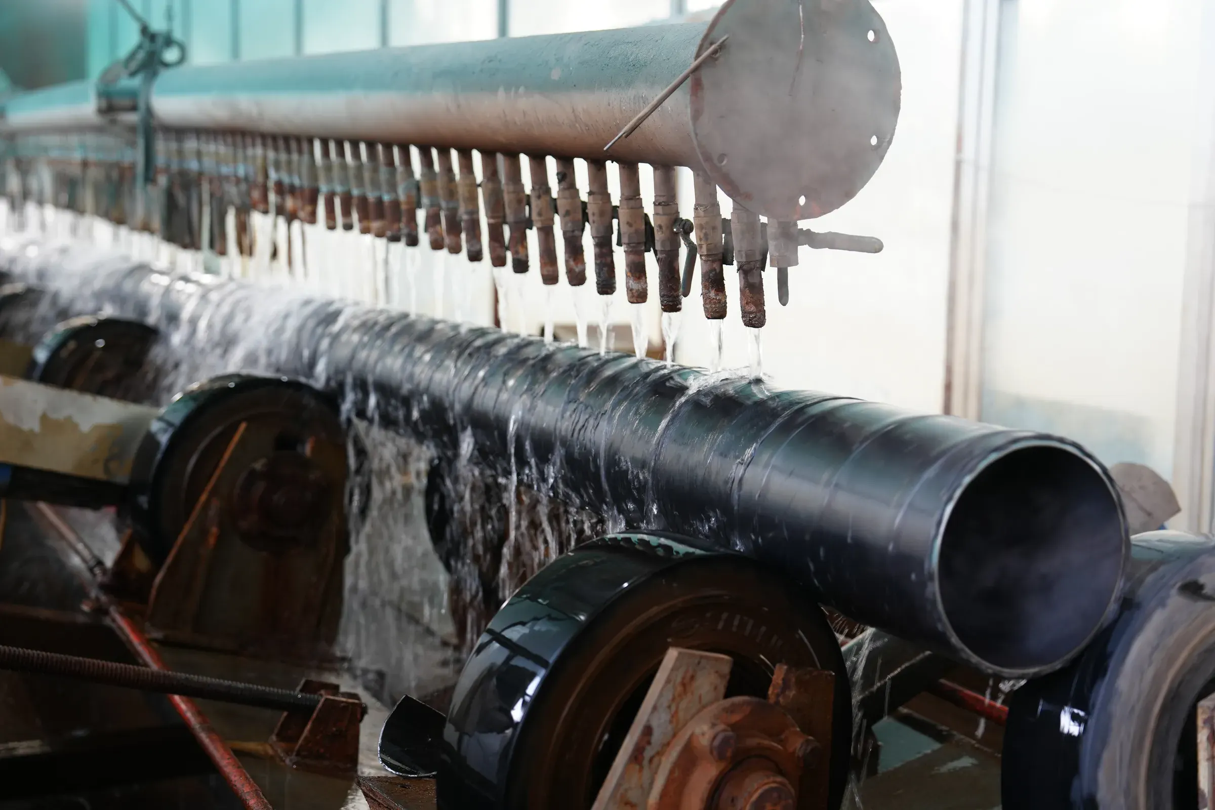Steel pipe on a roller line beneath water spray nozzles